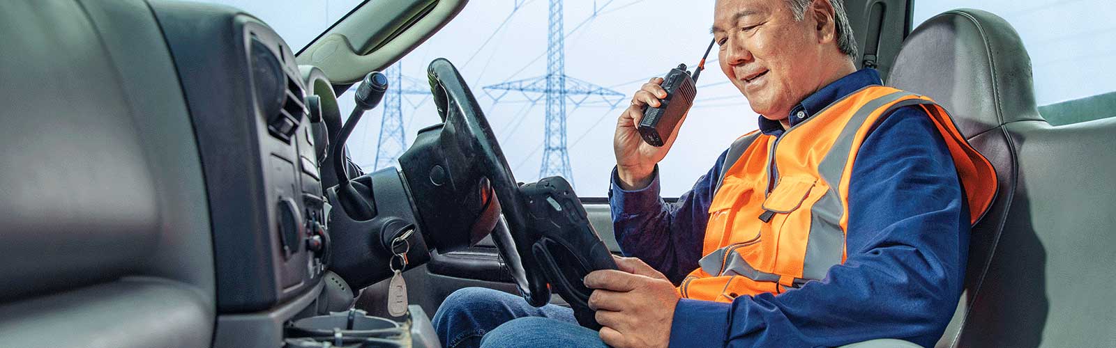 Man in truck wearing safety vest talks on walkie talkie