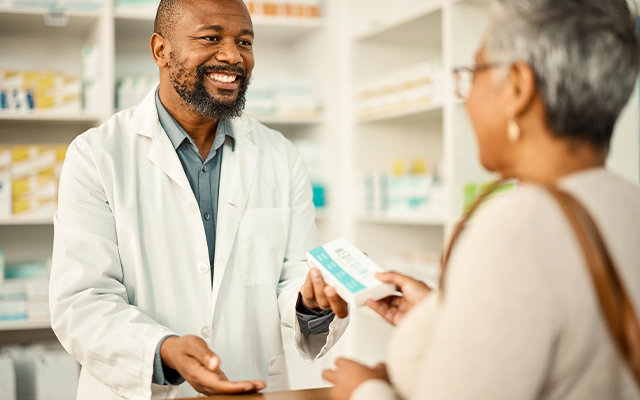 a pharmacist smiles as he give a customer her prescription