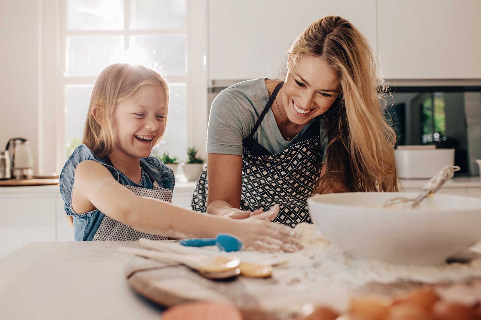 A mother and daughter laugh while baking in their kitchen.